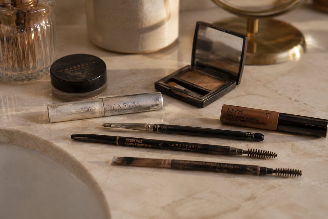 Collection of worn brow pencils and powders on bathroom counter — the daily routine powder brows replace — Kiss Kreations Tempe AZ